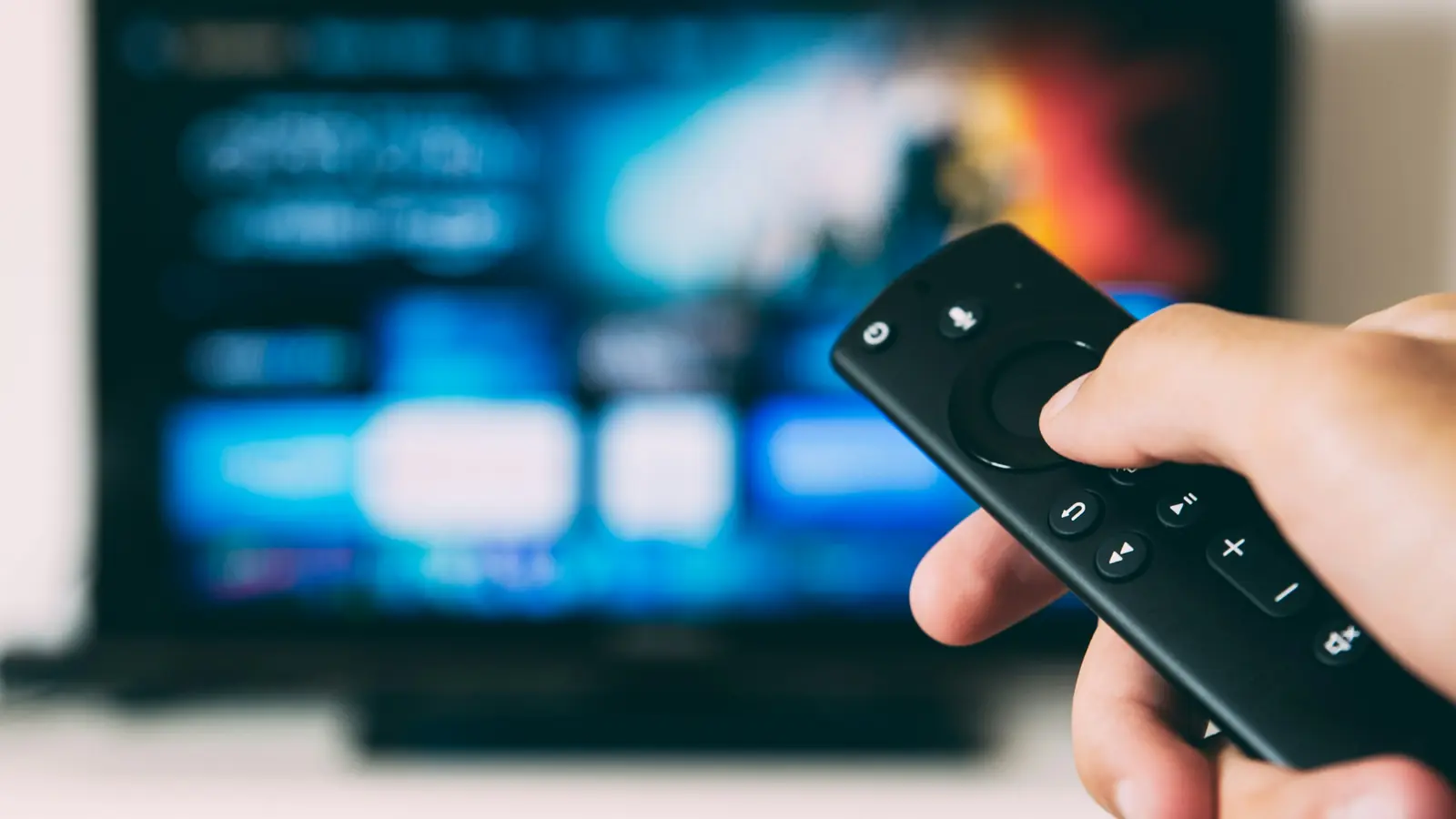 A hand holding a streaming-stick remote in front of a blue television screen
